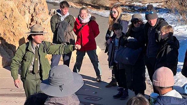 A group of park visitors listening to a ranger talk. The ranger is on the left within the group