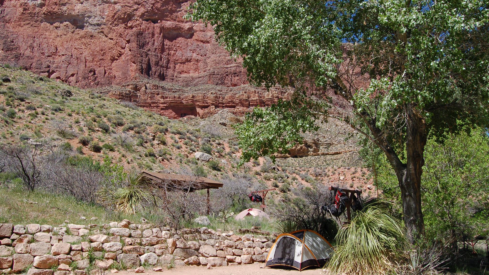 A creek with campsites on one side of the creek and several people with tents