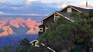 A brown building covered by trees with the Grand Canyon in the background.