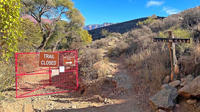 On a backcountry trail. an orange gate with a sign that reads, "Trail Closed".