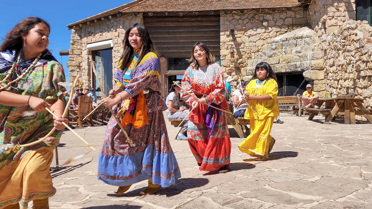 Blue skies above four young Yavapai-Apache Warriorettes in brightly colored regalia. 