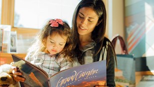 A woman is reading from a large picture book to her young daughter