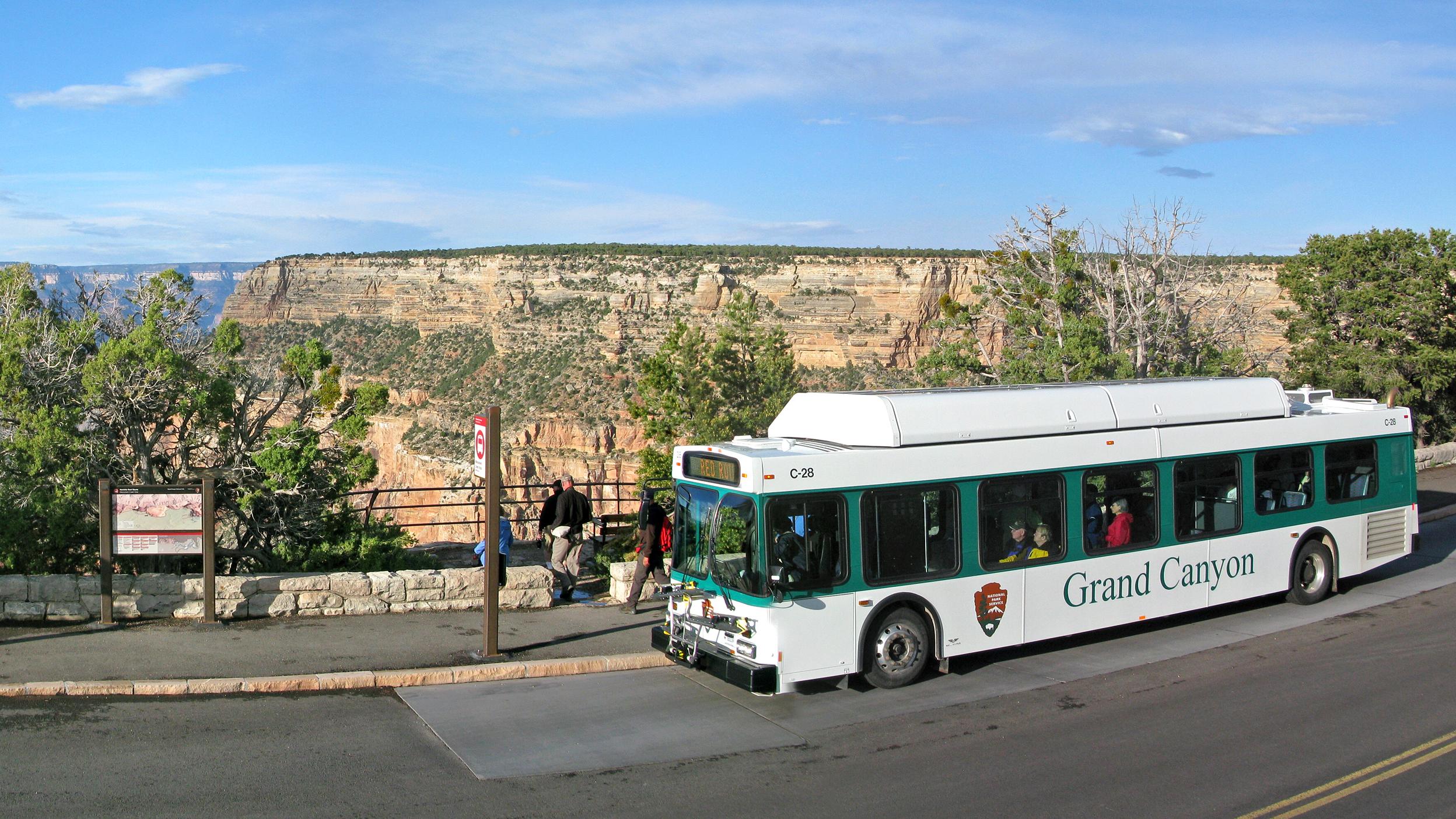 A green and white bus at a bus stop with a canyon landscape in the background