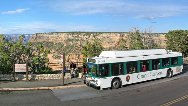 A green and white bus at a bus stop with a canyon landscape in the background