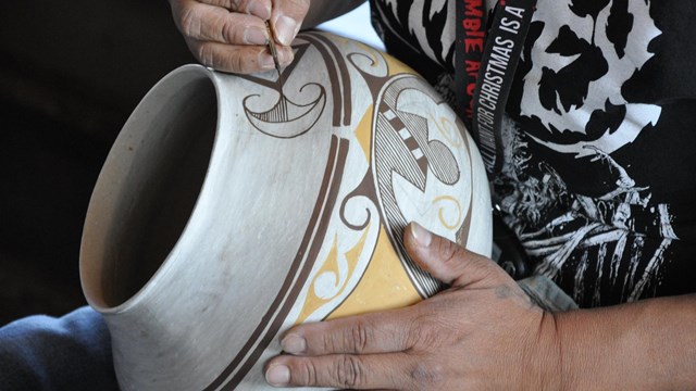 A woman paints a piece of pottery using traditional native designs. 