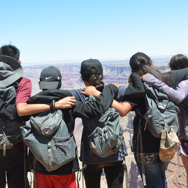 Students with arms over each others shoulders, look out over Grand Canyon