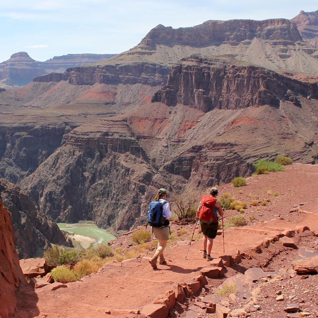Two hikers walking on a dirt trail. Beyond them the river within a steep granite gorge.
