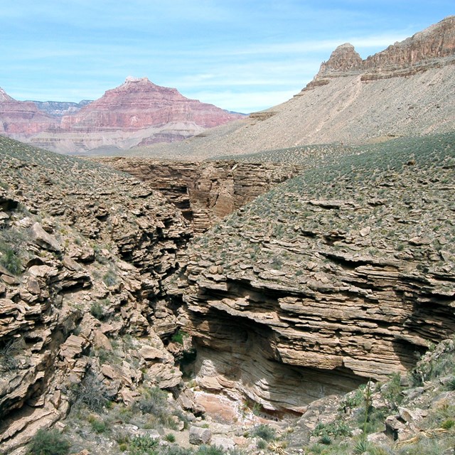 Green, grey, and tan thin rocks are stacked on top of each other, creating a green valley.