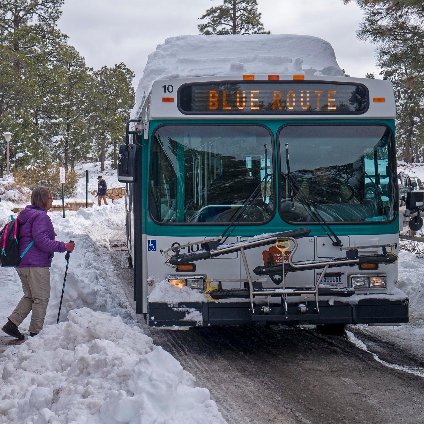 Surrounded by snow, a green and white bus boarding passengers at a bus stop 