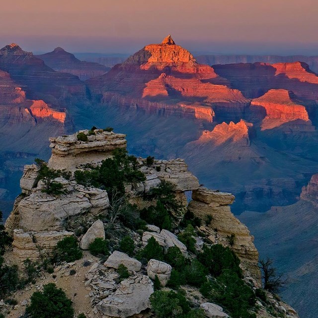 Jagged limestone pillars frame sunset-lit peaks in a vast canyon.