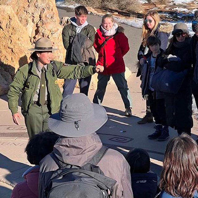 A group of park visitors listening to a ranger talk. The ranger is on the left within the group