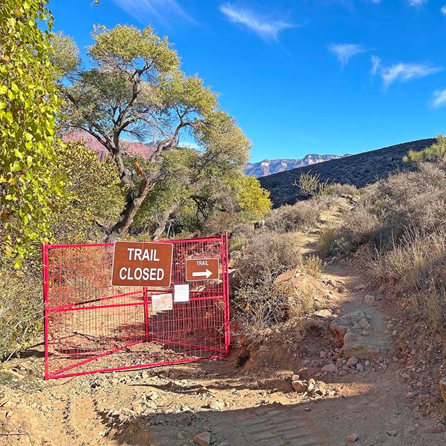 On a backcountry trail. an orange gate with a sign that reads, 