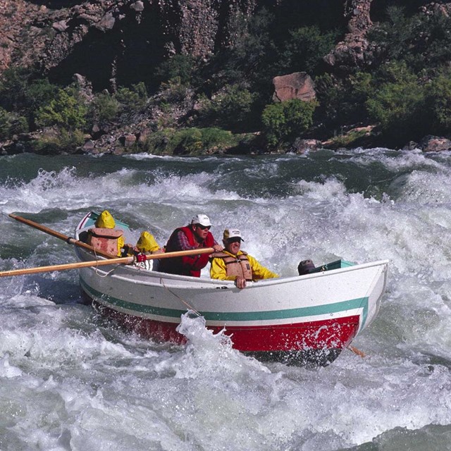 Four people in a wooden dory running a rapid