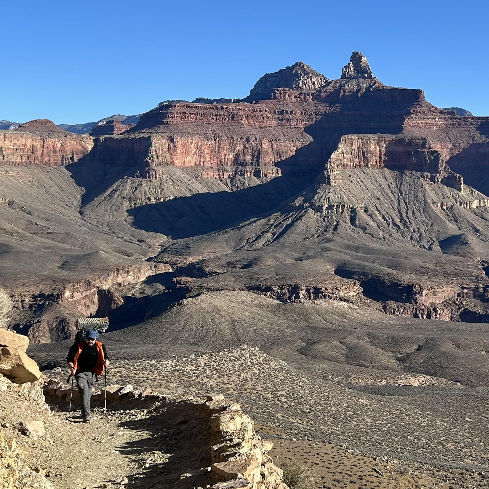 On a backcountry trail a hiker with a backpack walks uphill. 