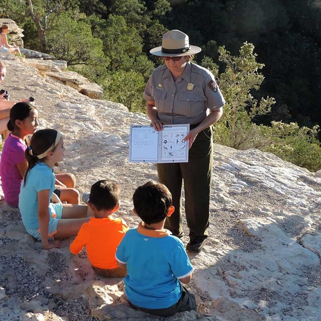 A ranger helps a group of four kids with there Junior Ranger book.