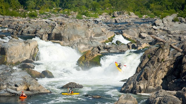 A kayaker going down a waterfall with two friends in kayaks waiting at the bottom.