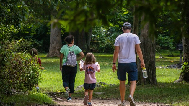 A family of four walks down a trail at Great Falls. A little girl holds open a Junior Ranger booklet