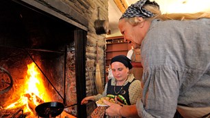 Two women cooking in the kitchen fireplace.