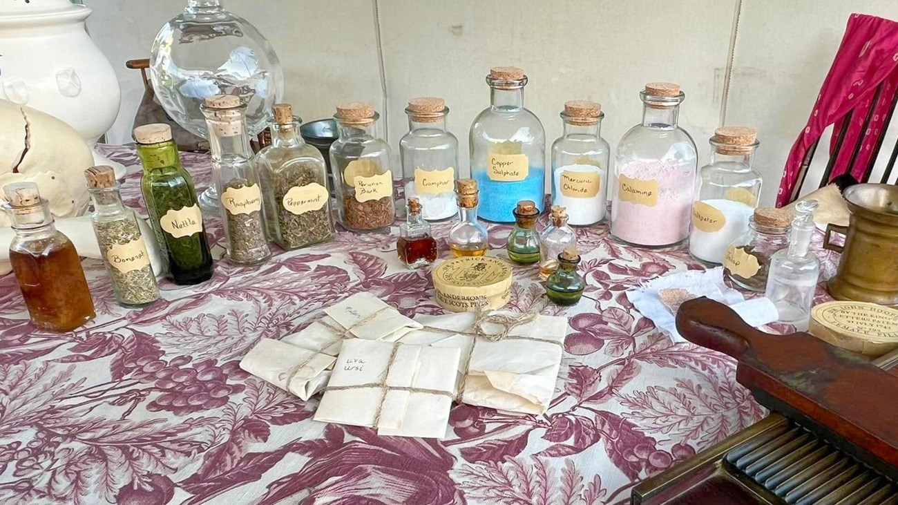 Historic herbs and powders in bottles on a patterned table cloth.