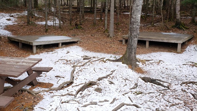 Wooden platforms and a picnic table in a snowy forest.