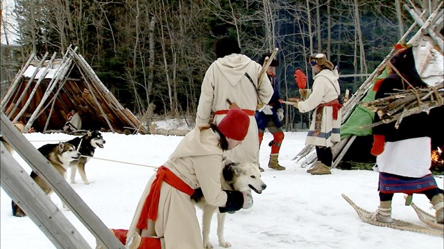 People dressed in historic winter clothing with dogs and snowshoes.