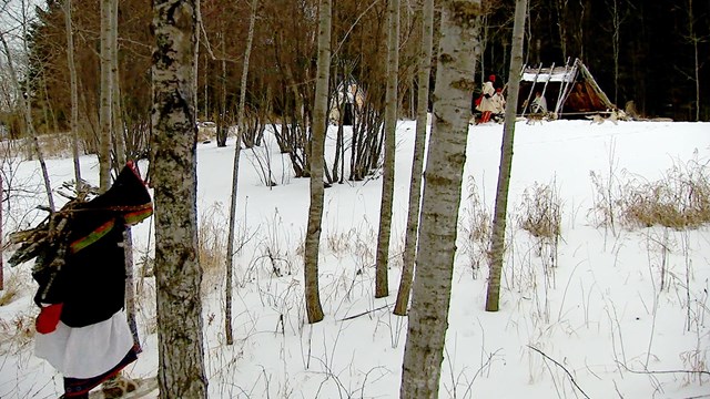 People in historic woolen blanket coats with snowshoes and sled dog team.