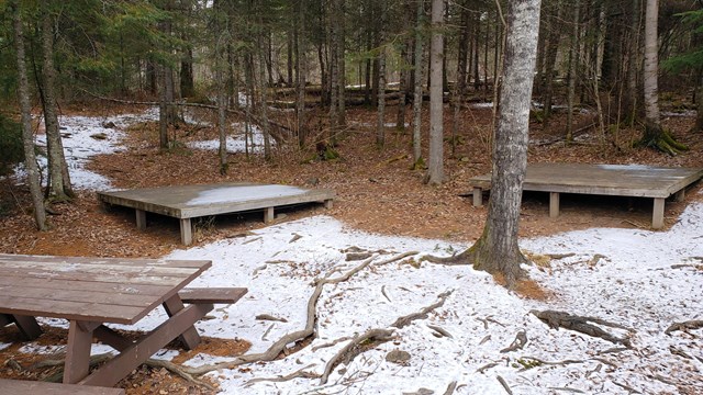 Wooden platforms and a picnic table in a snowy forest.