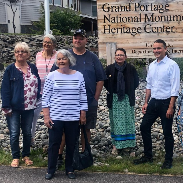 A group of people standing in front of the Grand Portage National Monument sign.