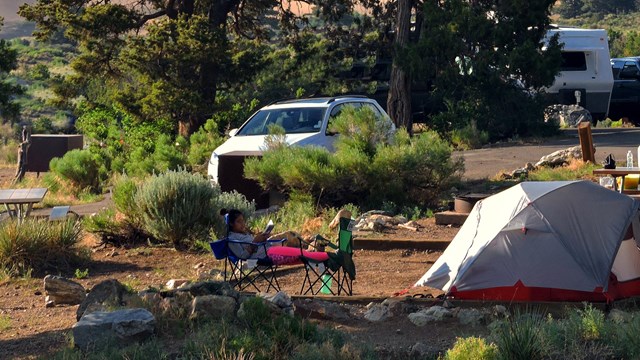 A woman relaxes at a campsite surrounded by trees, dunes and mountain