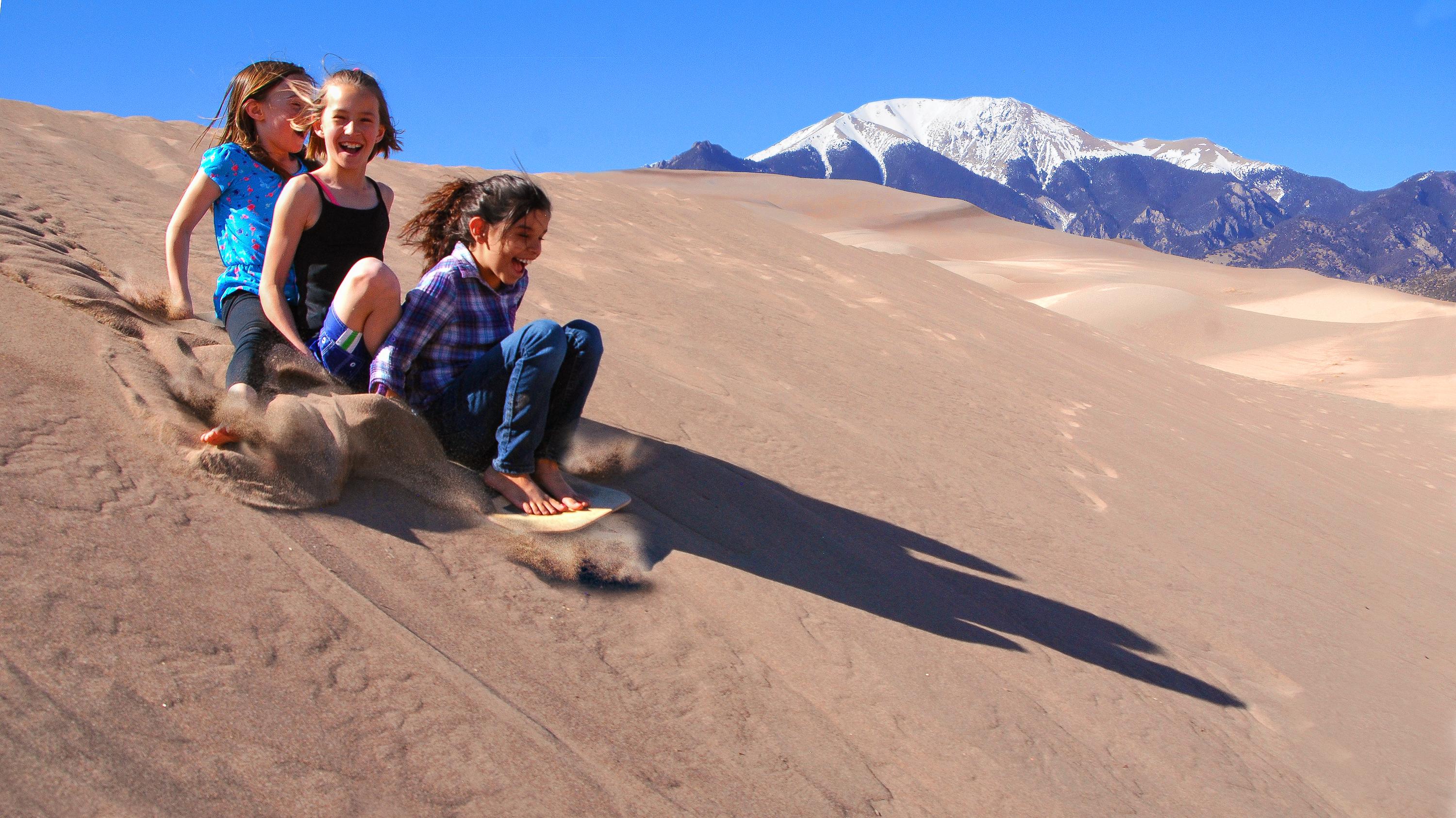 Teen girl and boy sliding down a dune on a sand sled