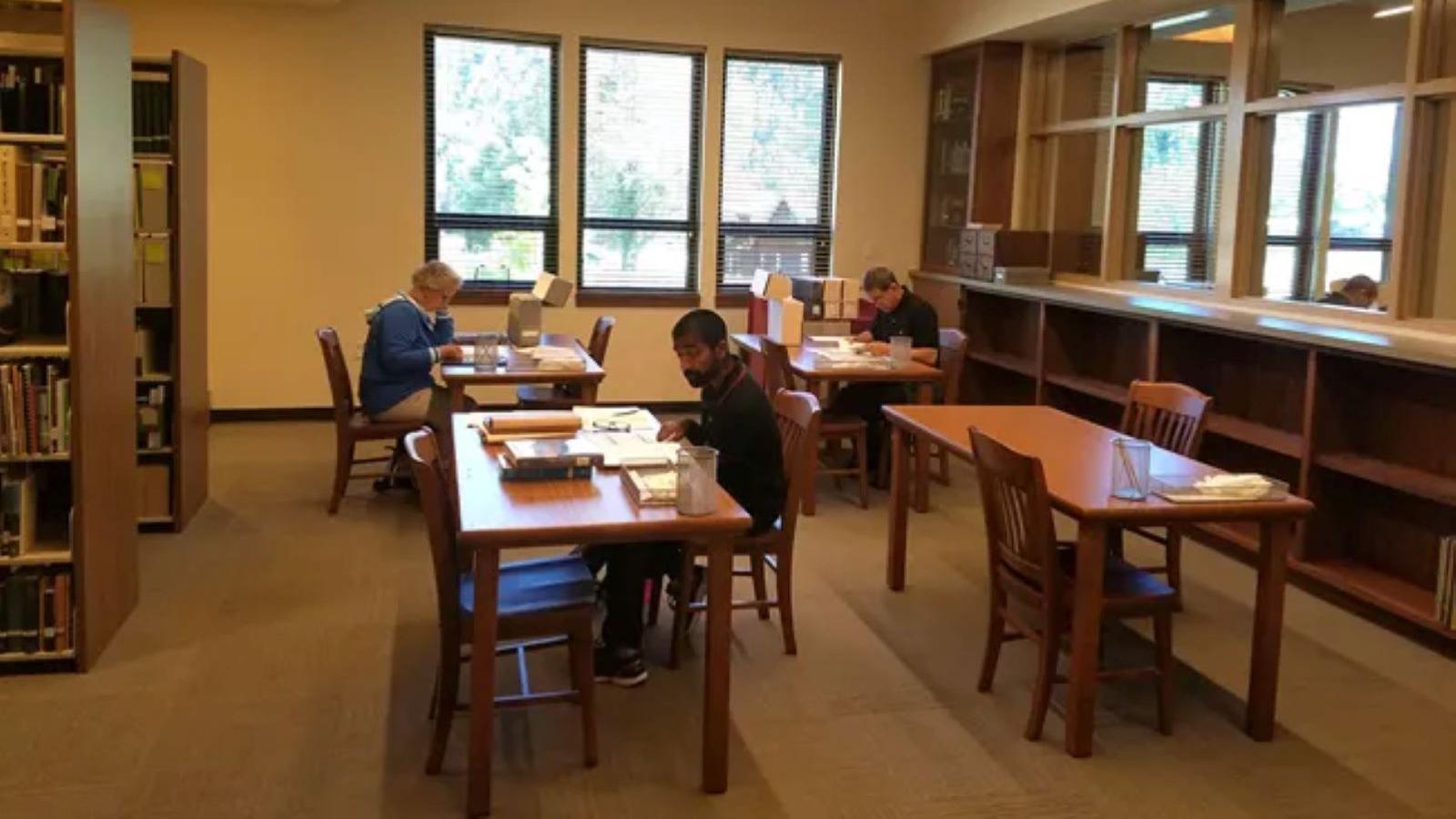 Three people at desks reading books and researching in a room.