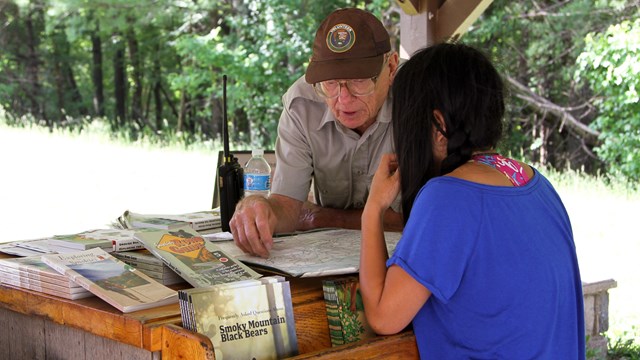 A volunteer in a safety vest with visitors and a book in hand
