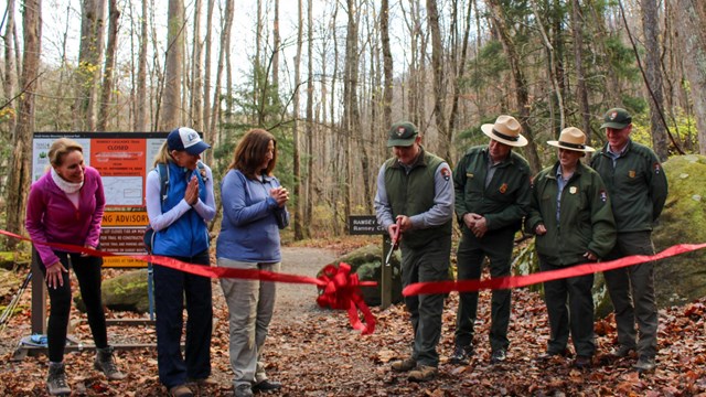 Ranger and partners on either side of a trail cutting a red ribbon across a trail.
