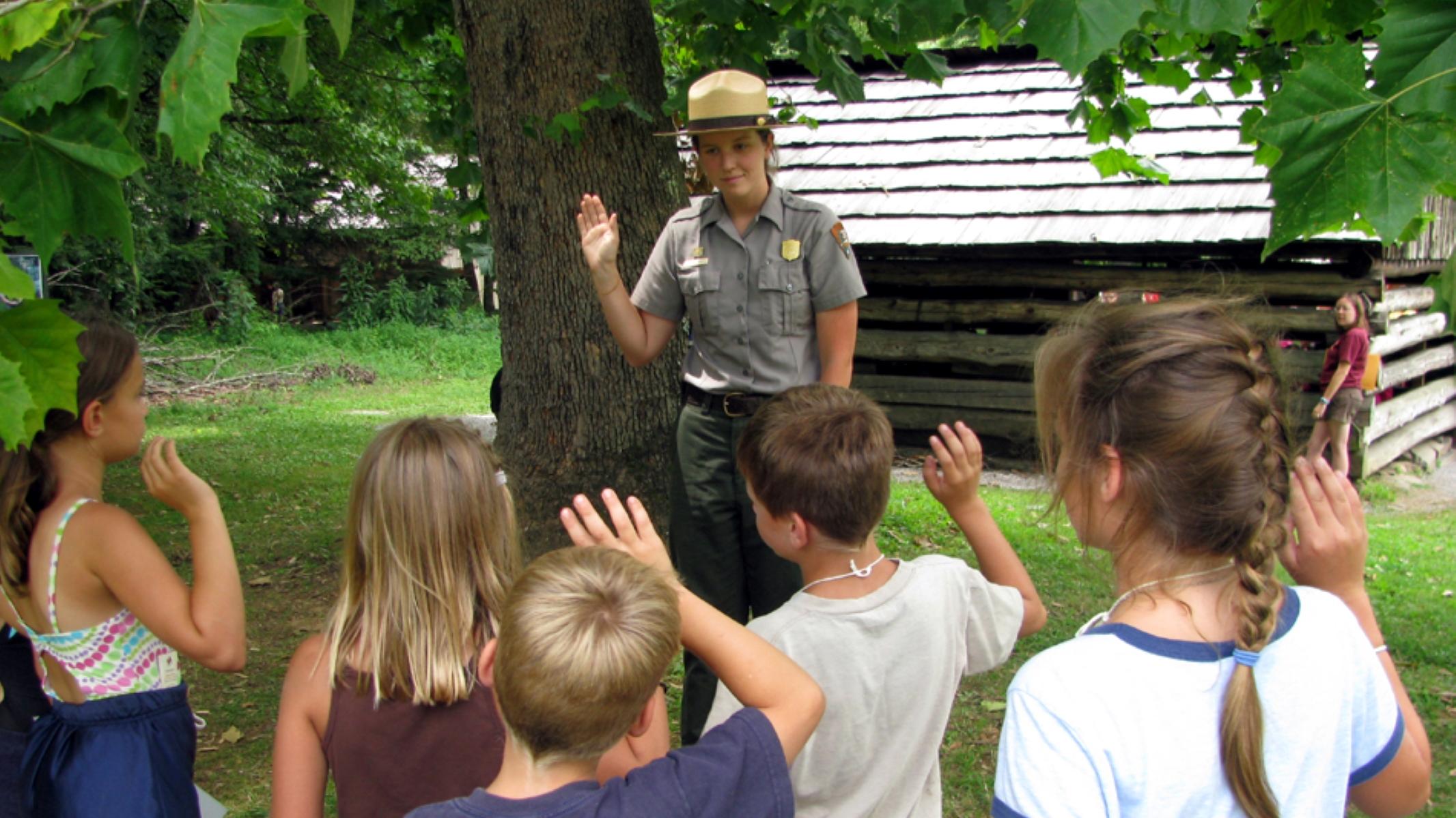A ranger near a cabin with children in a group facing them.