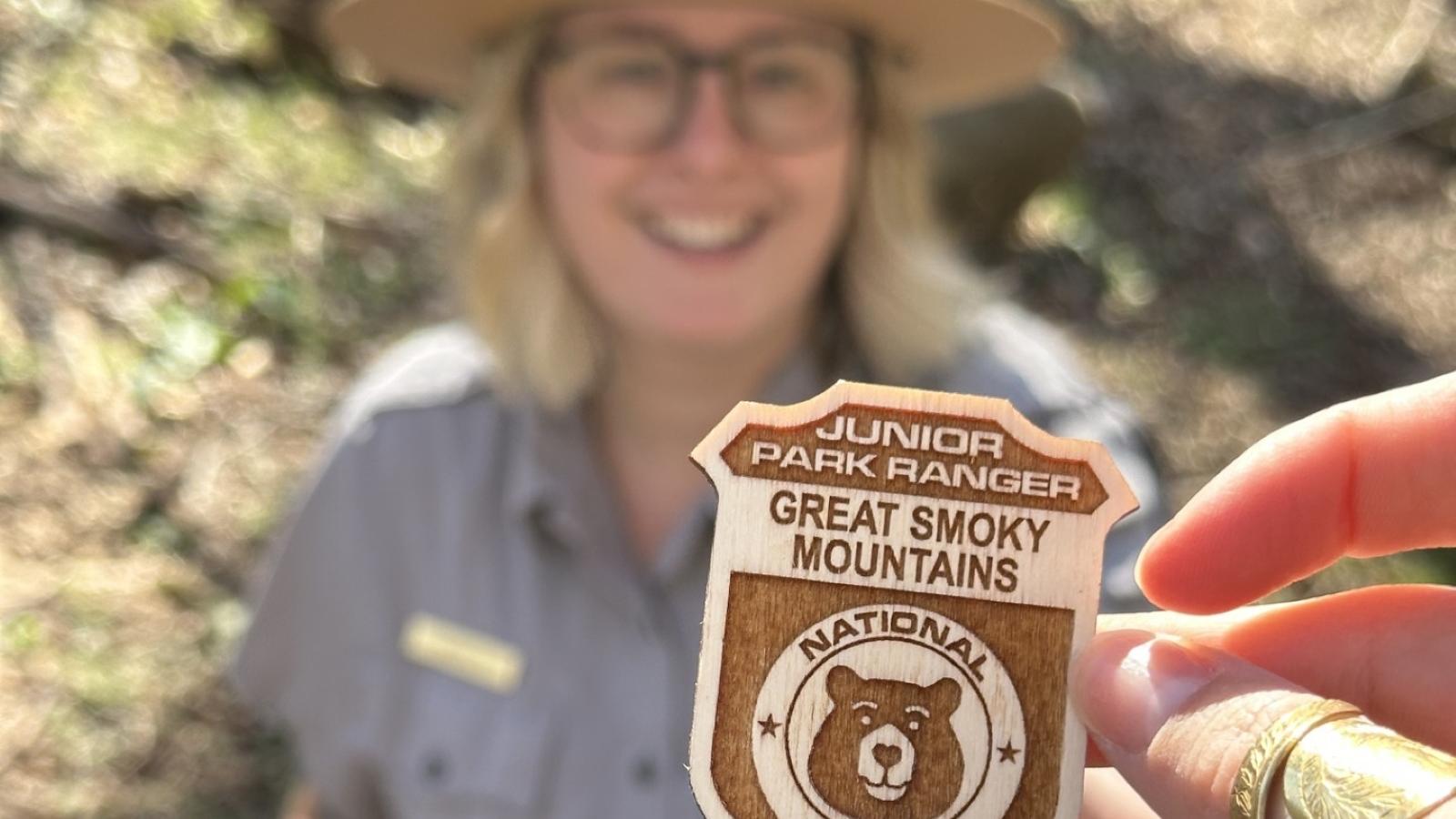 A jr ranger badge for great smoky mountains national park with a ranger behind it reaching for it.