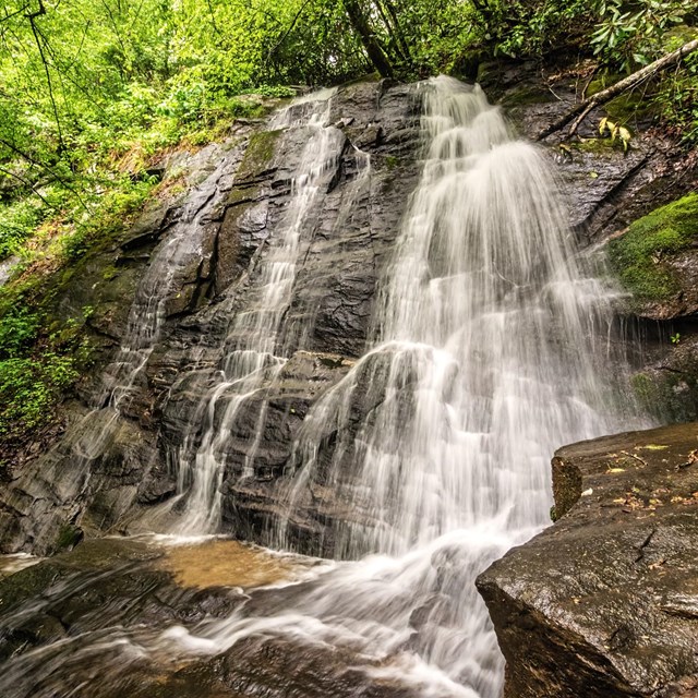 A fanning waterfall falling over rocks framed by green vegetation.