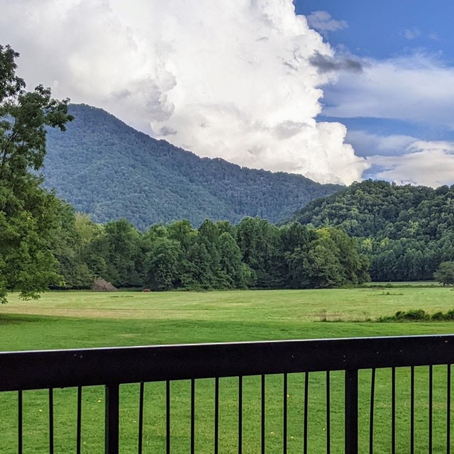 Rolling mountains above a grassy field. A porch railing in the foreground.