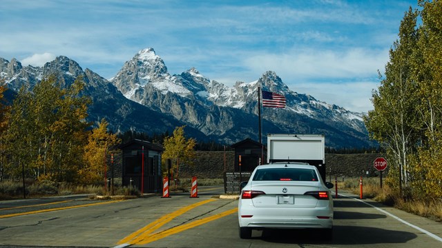 A car drives past a small booth with mountains in the distance.