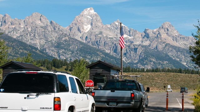 Cars wait an entrance station with mountains in the background