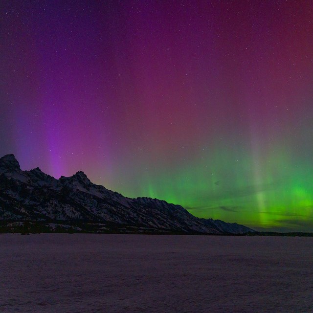 Stars and the Northern Lights visible over a silhouette of the Teton Range