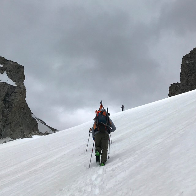 A researcher looks up at a peak in the Teton Range, surrounded by clouds