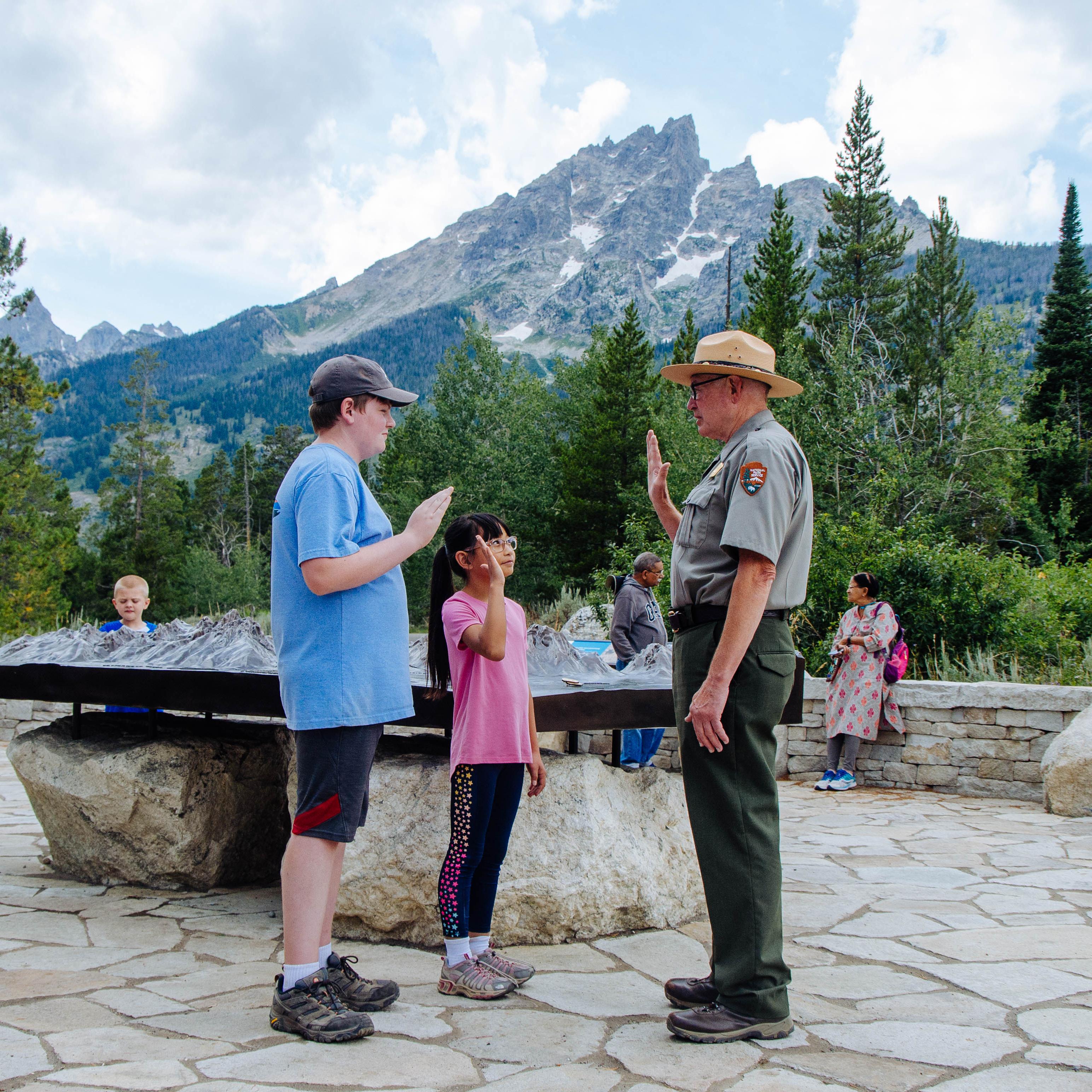 A ranger stands with two kids with a mountain in the background.