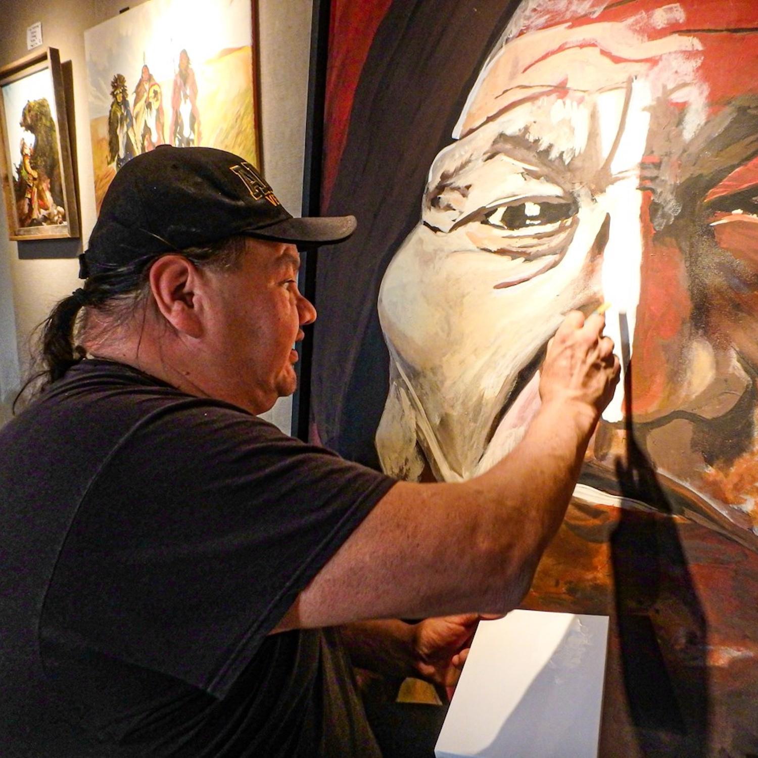 A seated man painting a large face on a canvas