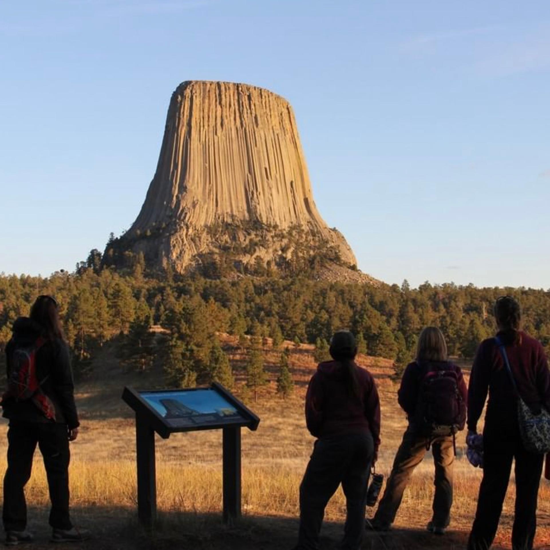 Devils Tower, a large rock monolith extending into the sky with visitors in foreground