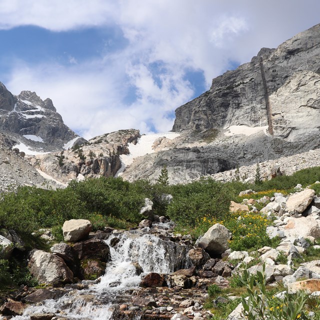 A creek flows through a canyon surrounded by granite mountain peaks