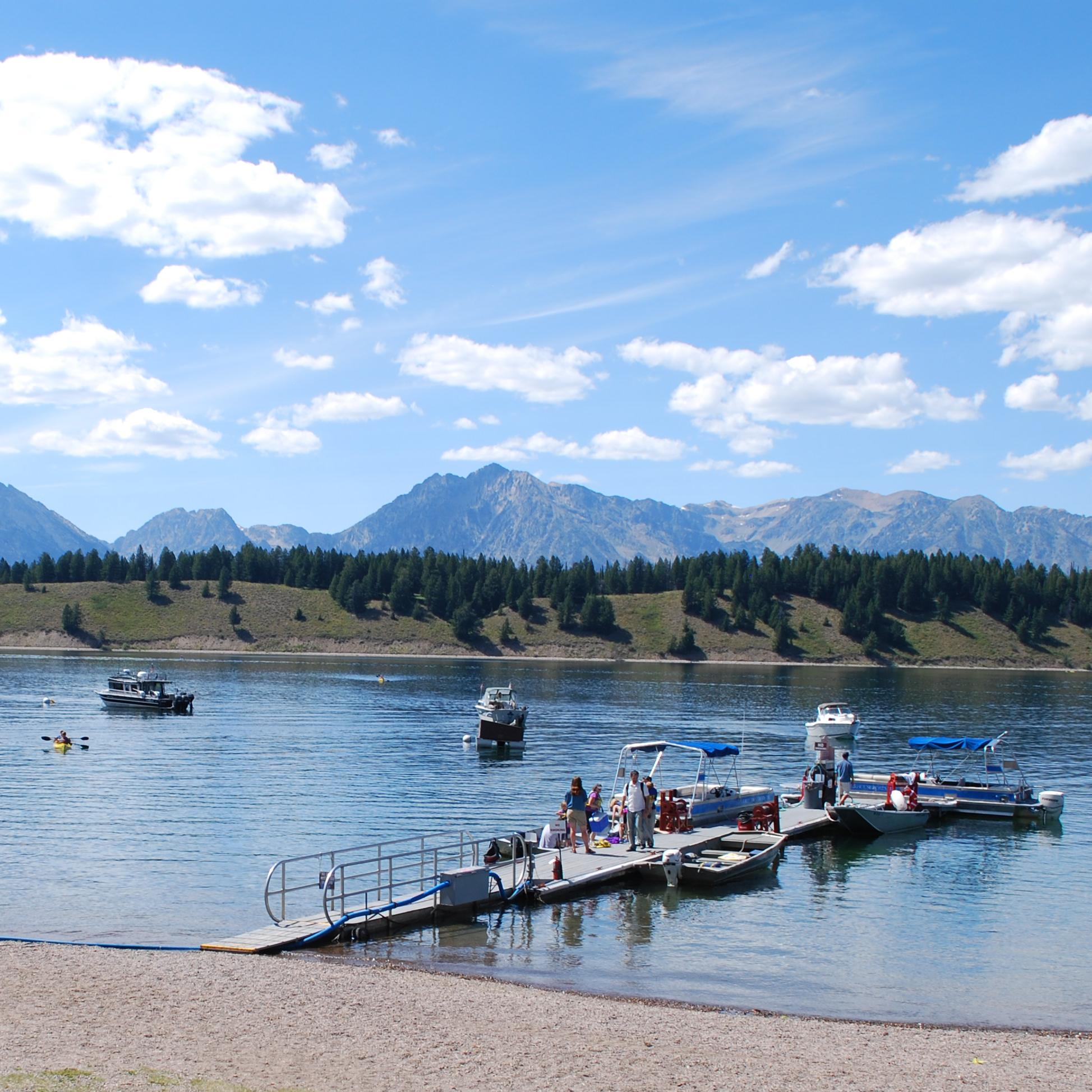 A dock with multiple boats on a lake with mountains in the background.