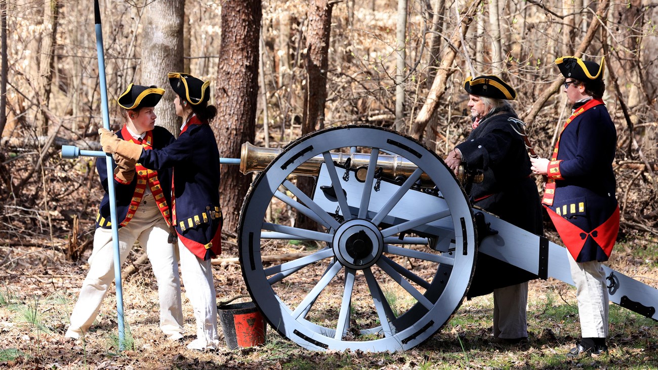 A bronze six-pound cannon is being loaded. Four gunners in blue coats surround the piece.