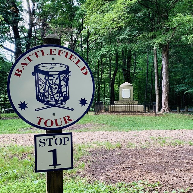 Battlefield Tour stop sign in front of monument and path in woods