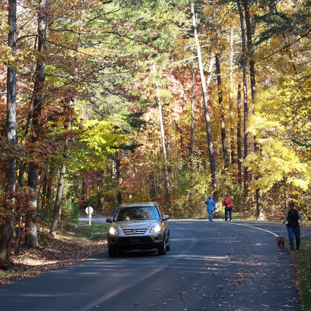 A car drives on the tour road, people are walking on the opposite side