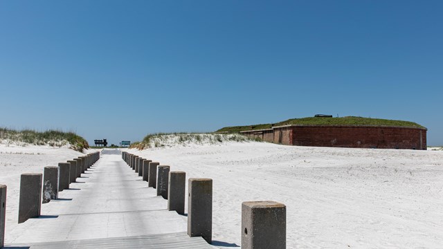 A colorful sailboat is beached in front of a large brick fort.